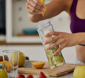 unrecognizable sportswoman using lemon while making fruit smoothie home